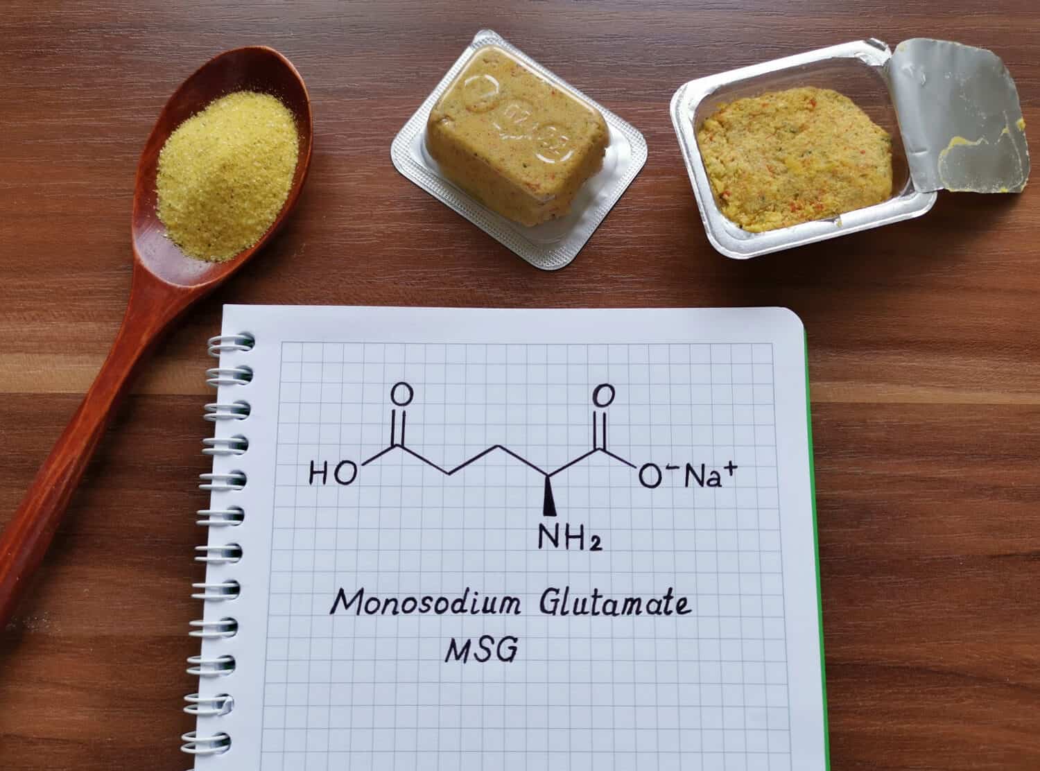 Structural chemical formula of monosodium glutamate (or MSG) with spoonful of a yellow, dry, seasoning spice mix and bouillon cubes. MSG is used in cooking as a flavor enhancer in many food.