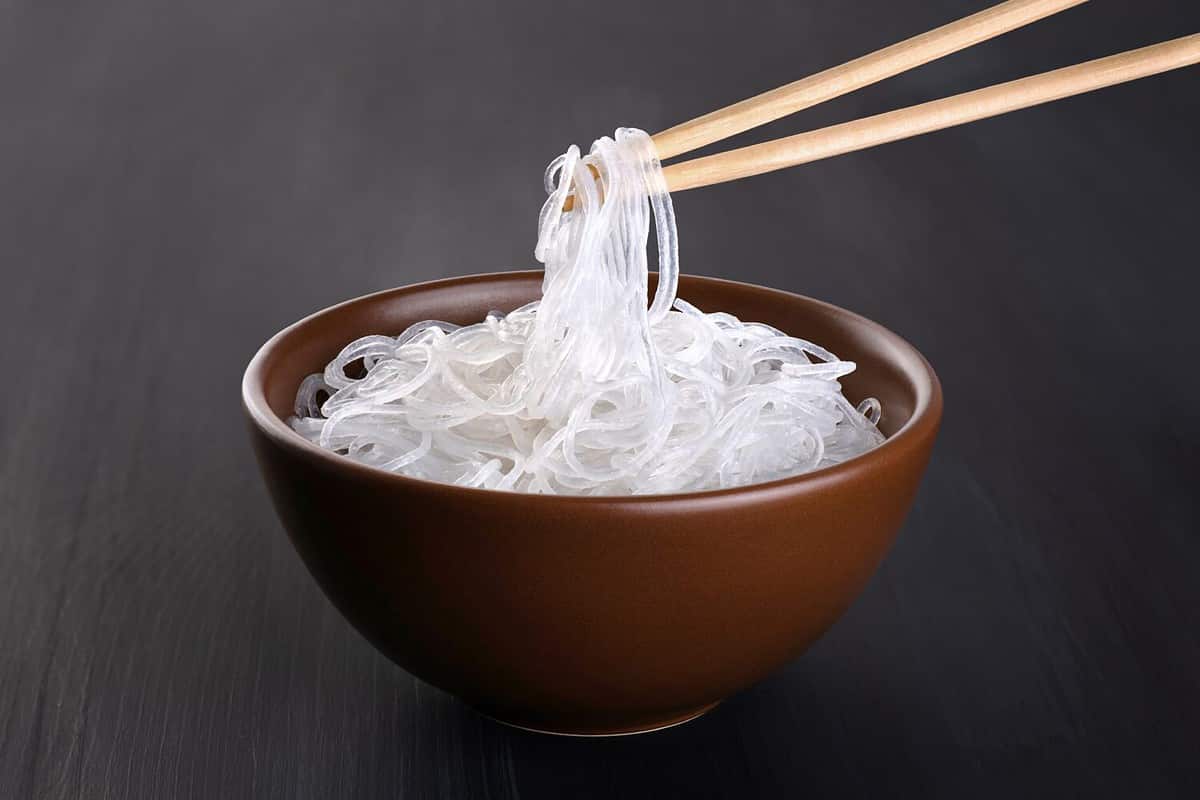 Rice glass noodles in a bowl on a dark background. Chopsticks holding noodles. With clipping path.