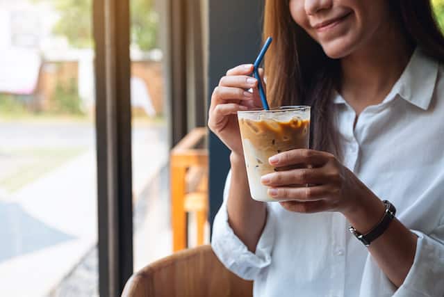 Closeup image of a beautiful young asian woman holding and drinking iced coffee