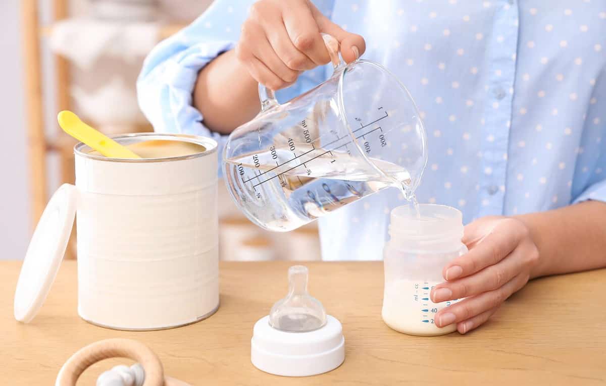 Woman preparing infant formula at table indoors, closeup. Baby milk