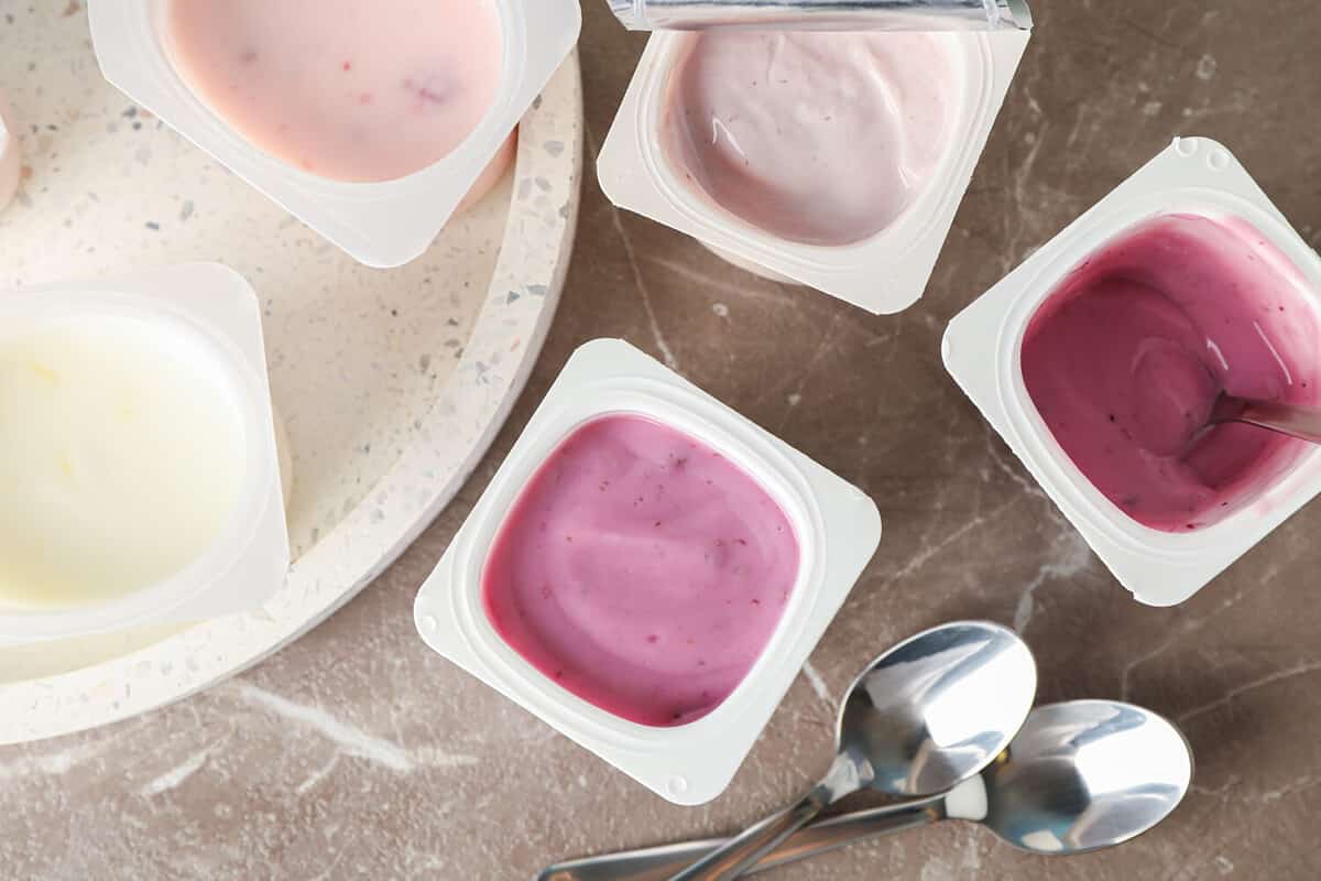 Composition with plastic cups with yogurt on grey table