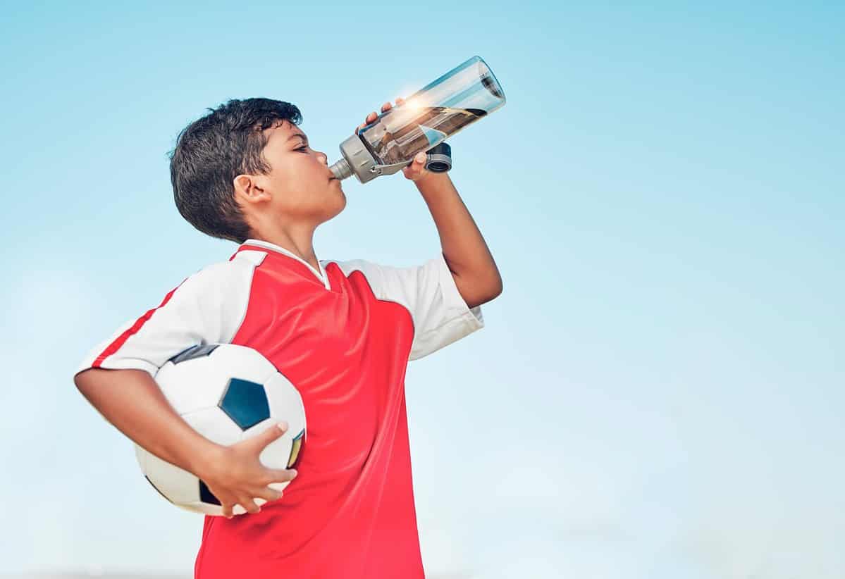 Training, sports and football with child drinking water for fitness, health or endurance exercise. Wellness, summer and workout with young soccer player and bottle for electrolytes, relax and thirsty