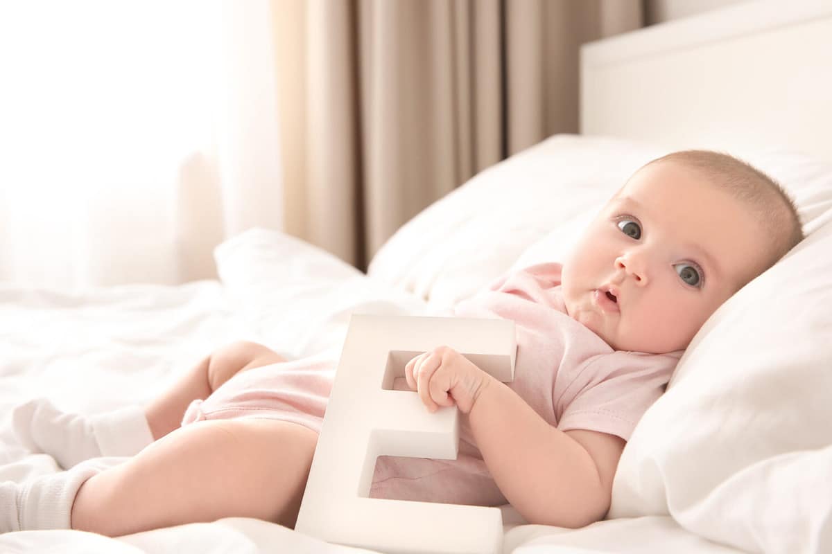 Cute little baby with letter E lying on bed. Choosing name concept