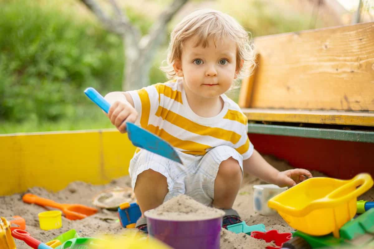 A little boy playing in the sandbox at the playground outdoors. Toddler playing with sand molds and making mudpies. Outdoor creative activities for kids.