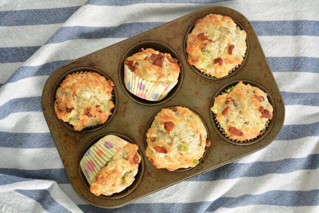 Fresh baked bacon cheddar muffins in old muffin tin on blue and whit striped teacloth in flat lay composition. Healthy breakfast or snack.