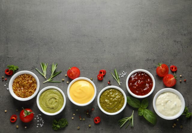 Bowls with different sauces and ingredients on gray background, flat lay. Space for text