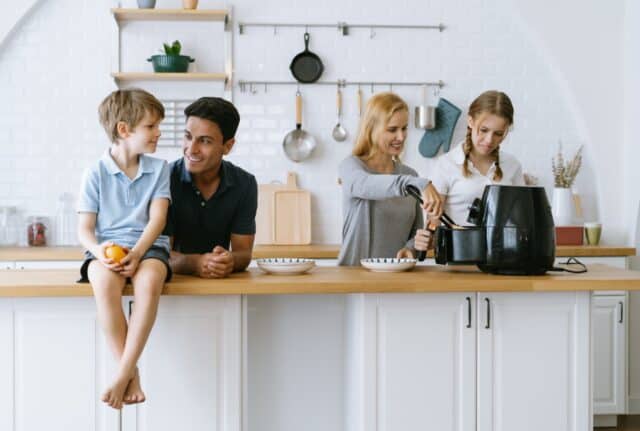 Happy family cooking morning breakfast together in kitchen at home. Mother and daughter cooking toast bread by Air Fryer machine to father and son. Home recreation and food preparation on weekend.