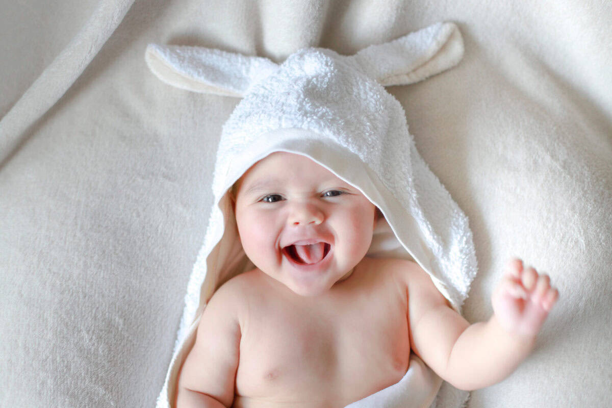Adorable newborn baby wrap by white rabbit towel with smiling face. Happy mixed race Asian-German boy drying after bathing