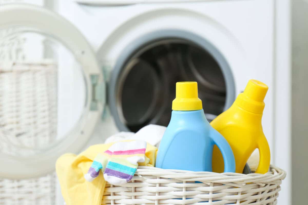 Bottles of detergent and children's clothes in wicker basket near washing machine indoors