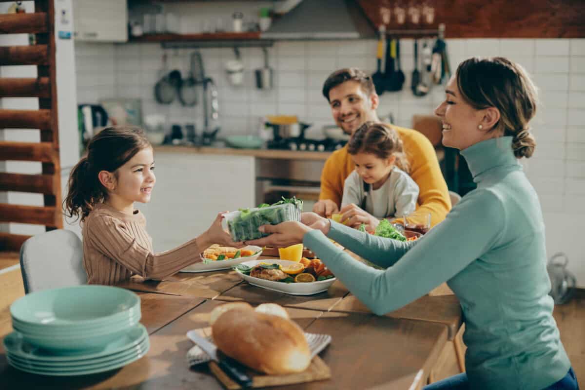 Happy mother passing salad to her daughter during family lunch in dining room.