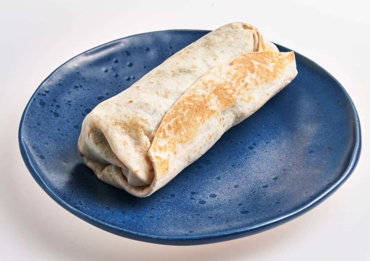 A fresh burrito wrapped tightly and served on a blue ceramic plate against a white background.