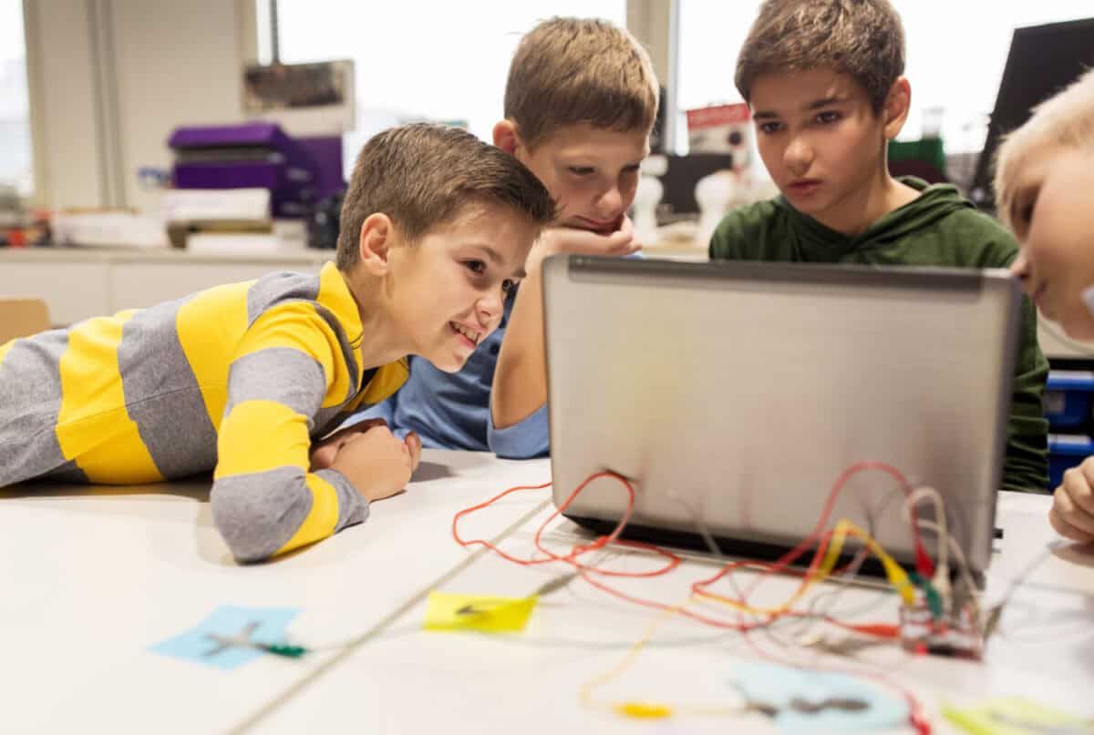 education, children, technology, science and people concept - group of happy kids with laptop computer playing with invention kit at robotics school lesson