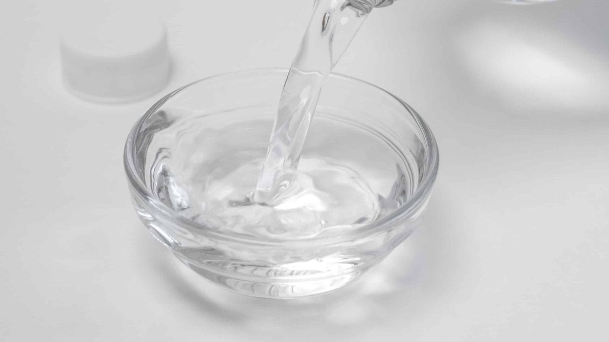 Vinegar being poured from a bottle into a glass bowl. 5 steps to kill weeds with vinegar.