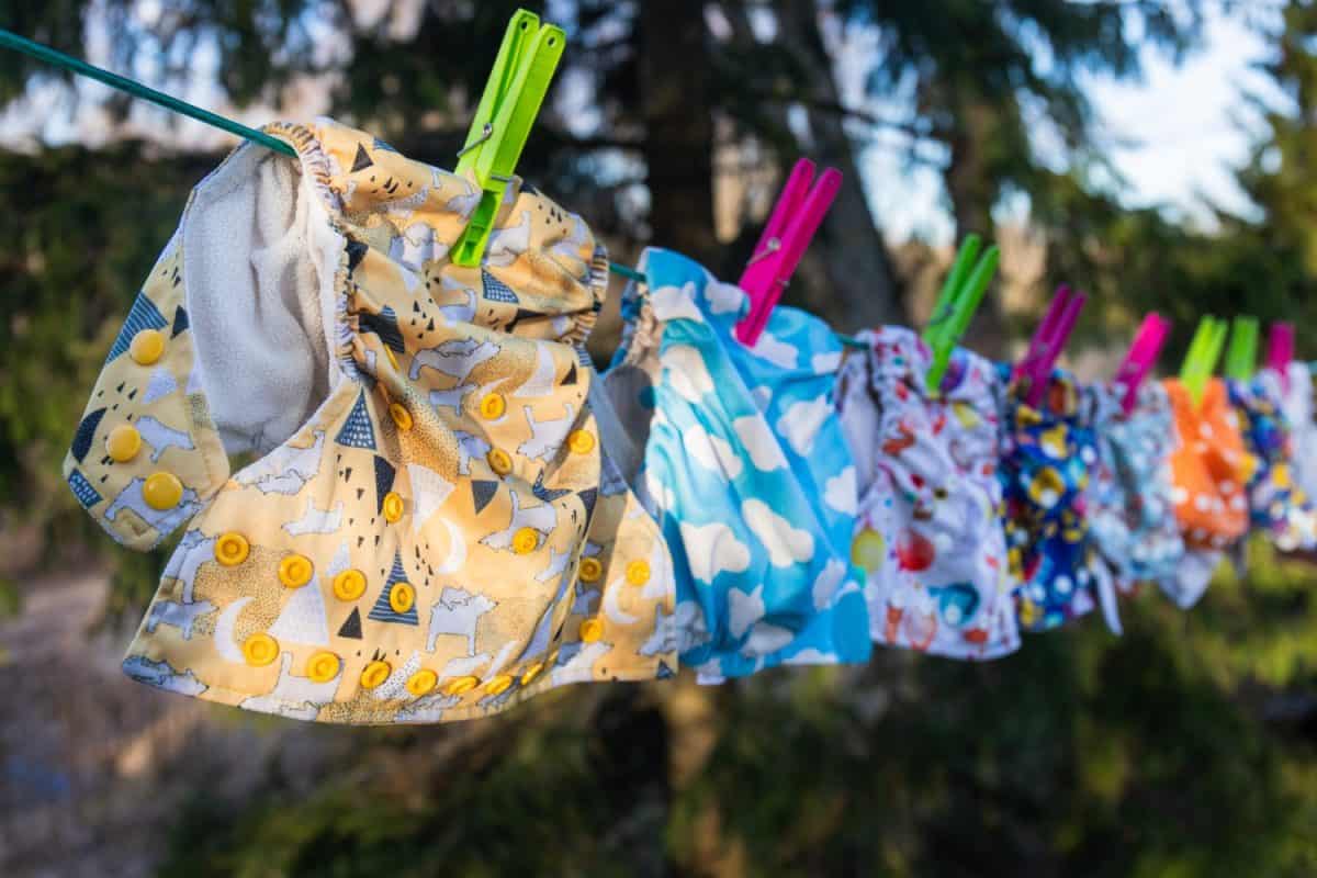 Cloth diapers dry in the sun on a full clothesline - laundry day! Reusable baby diapers in front of a nature background and blue sky. Eco friendly nappies, Sustainable lifestyle. Zero waste concept. Best treatment for diaper rash