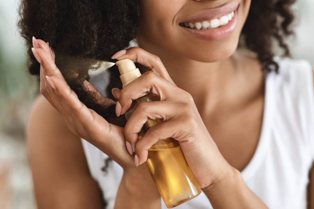 Split Ends Repair Treatment. Smiling African Woman Applying Essential Oil Spray On Her Curly Brown Hair At Home, Cropped Image, Closeup. Shampoo for extremely dry hair