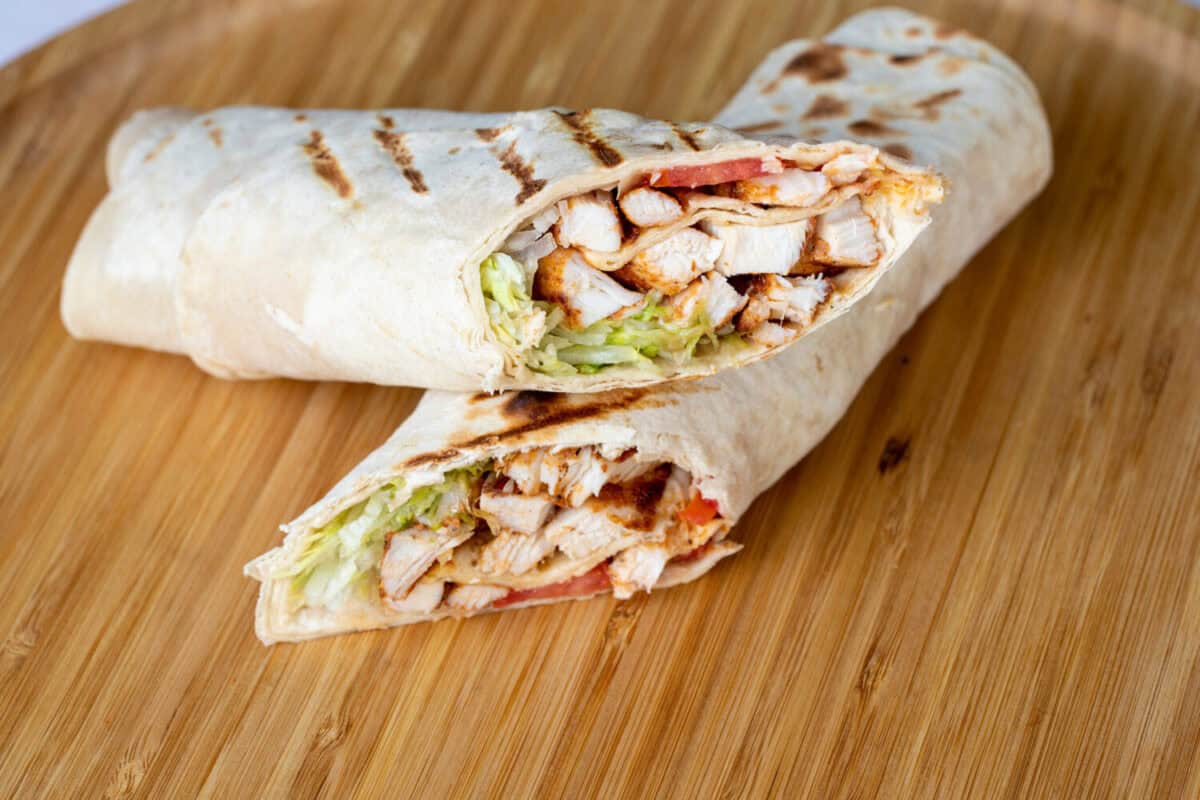 Healthy lunch snack. Stack of mexican street food fajita tortilla wraps with grilled buffalo chicken fillet and fresh vegetables, light grey background copy space