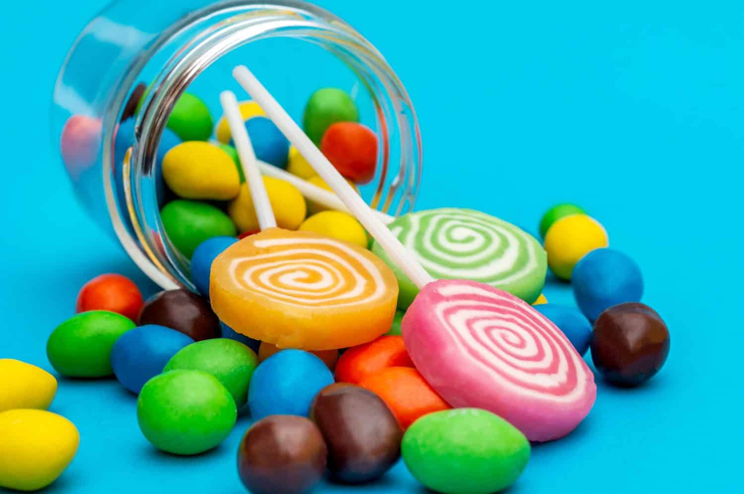 Candies scattered from glass jar on blue background. Close up.