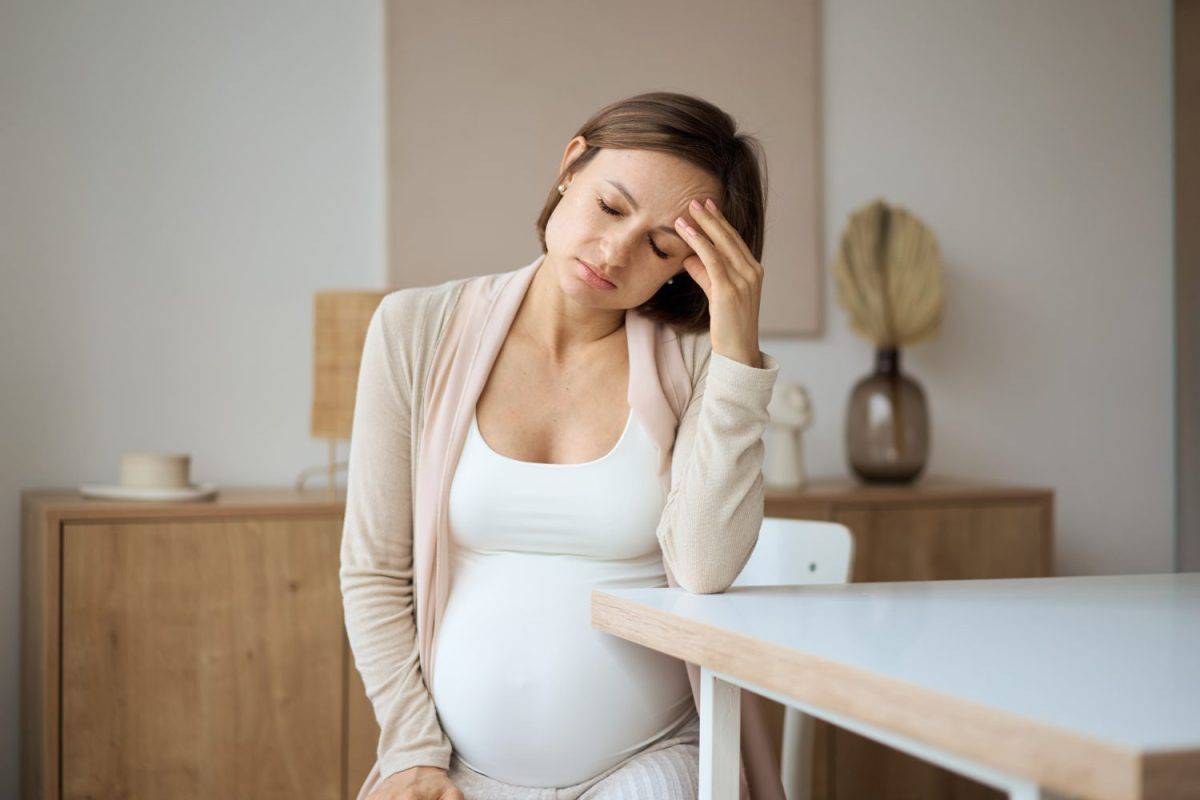 Pregnant woman suffering from headaches while sitting at the table. High quality photo. Pregnancy Symptoms No One Warns You About