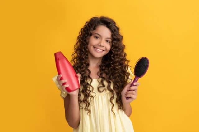 happy child with long curly hair hold shampoo bottle and hairbrush, hair