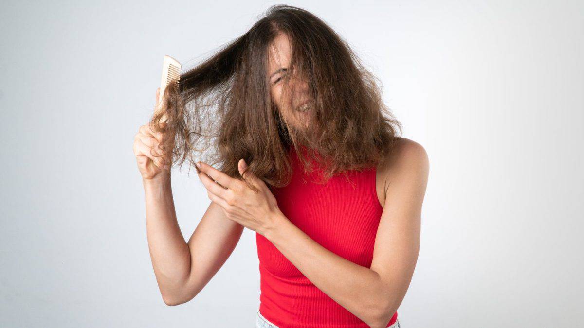 It hurts a woman when combing naughty, tangled hair - pulling out a comb and pulling her hair. High quality photo. Shampoos for extremely dry hair