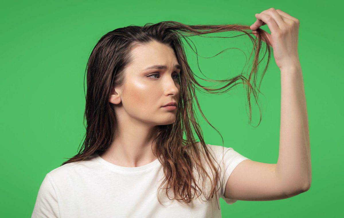 Attractive young woman is sad about her dirty, oily and greasy hair, isolated on a green background. Need a shampoo concept. Easily removable and replaceable chroma key background. Shampoo for oily hair