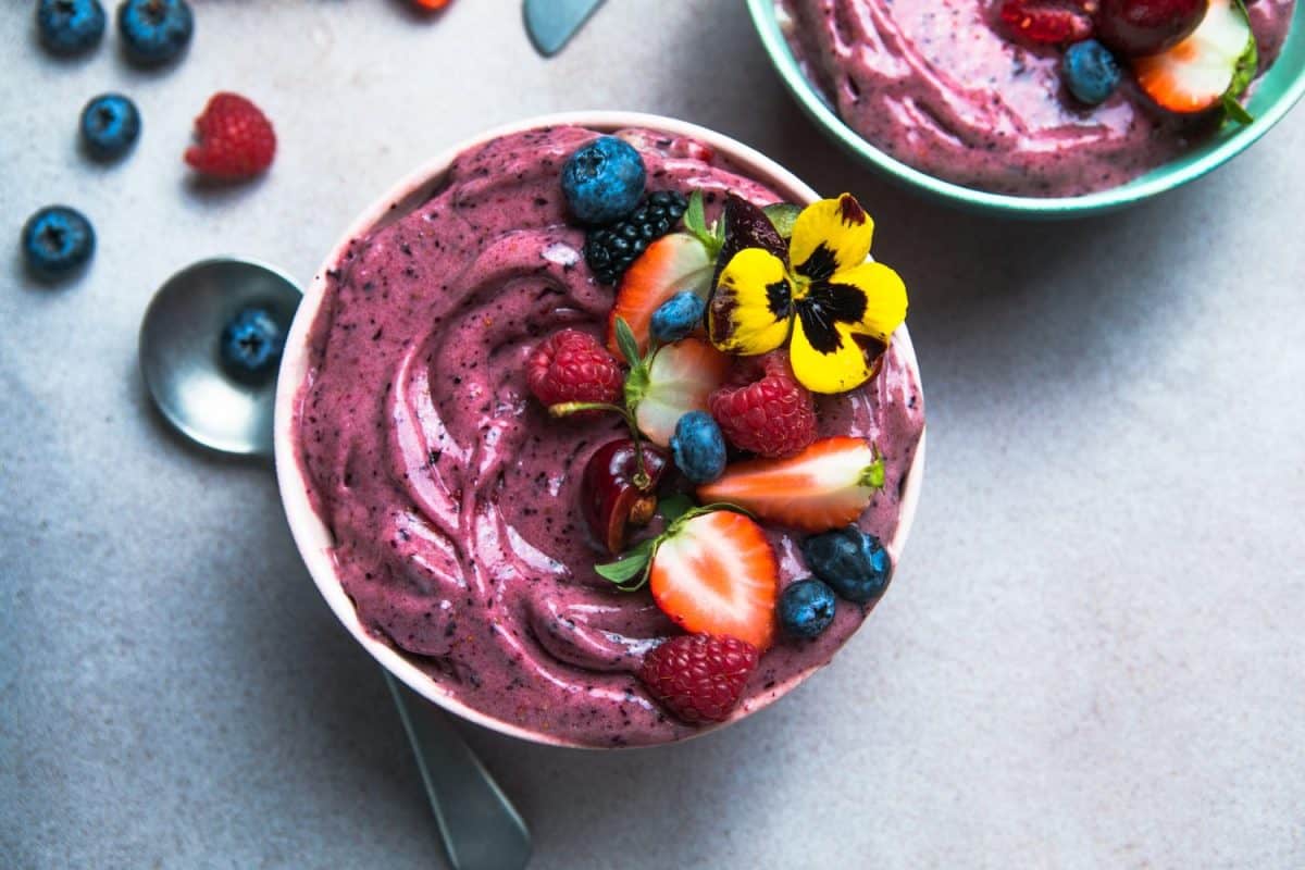 Two summer acai smoothie bowls with strawberries, blueberries, on gray concrete background. Breakfast bowl with fruit and cereal, close-up, top view, healthy food