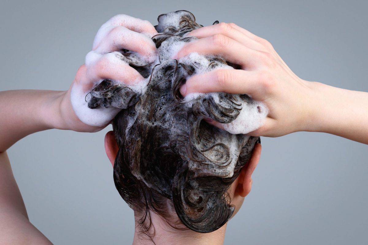 Hair washing procedure. A young girl washing her hair with a shampoo for oily hair on a gray background.
