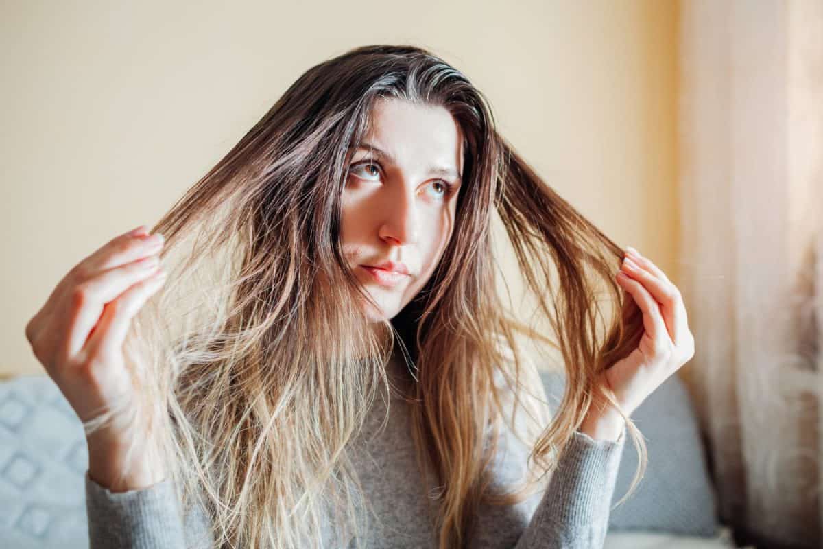 Young annoyed woman is upset about dirty oily and greasy hair touching it at home. Health treatment. Hair care products. Selfcare. Shampoo for oily hair