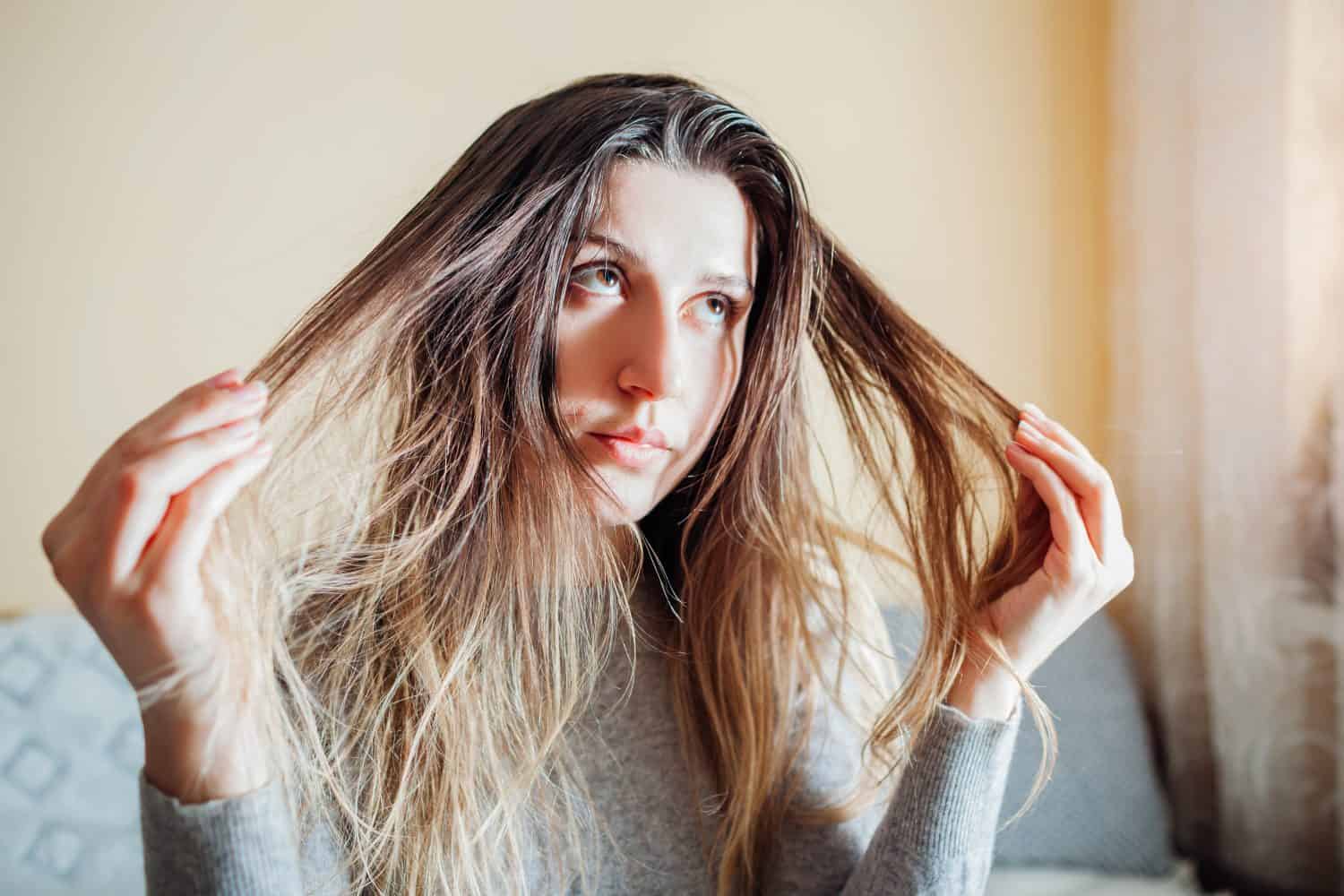 Young annoyed woman is upset about dirty oily and greasy hair touching it at home. Health treatment. Hair care products. Selfcare. Shampoo for oily hair