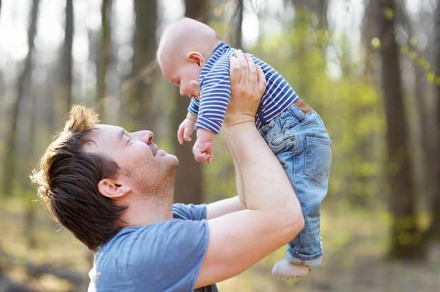 Proud father playing with his newborn son during walking in the park. Happy middle age man tossing his little baby in the air. Parenthood. Involved dad taking care of his infant son