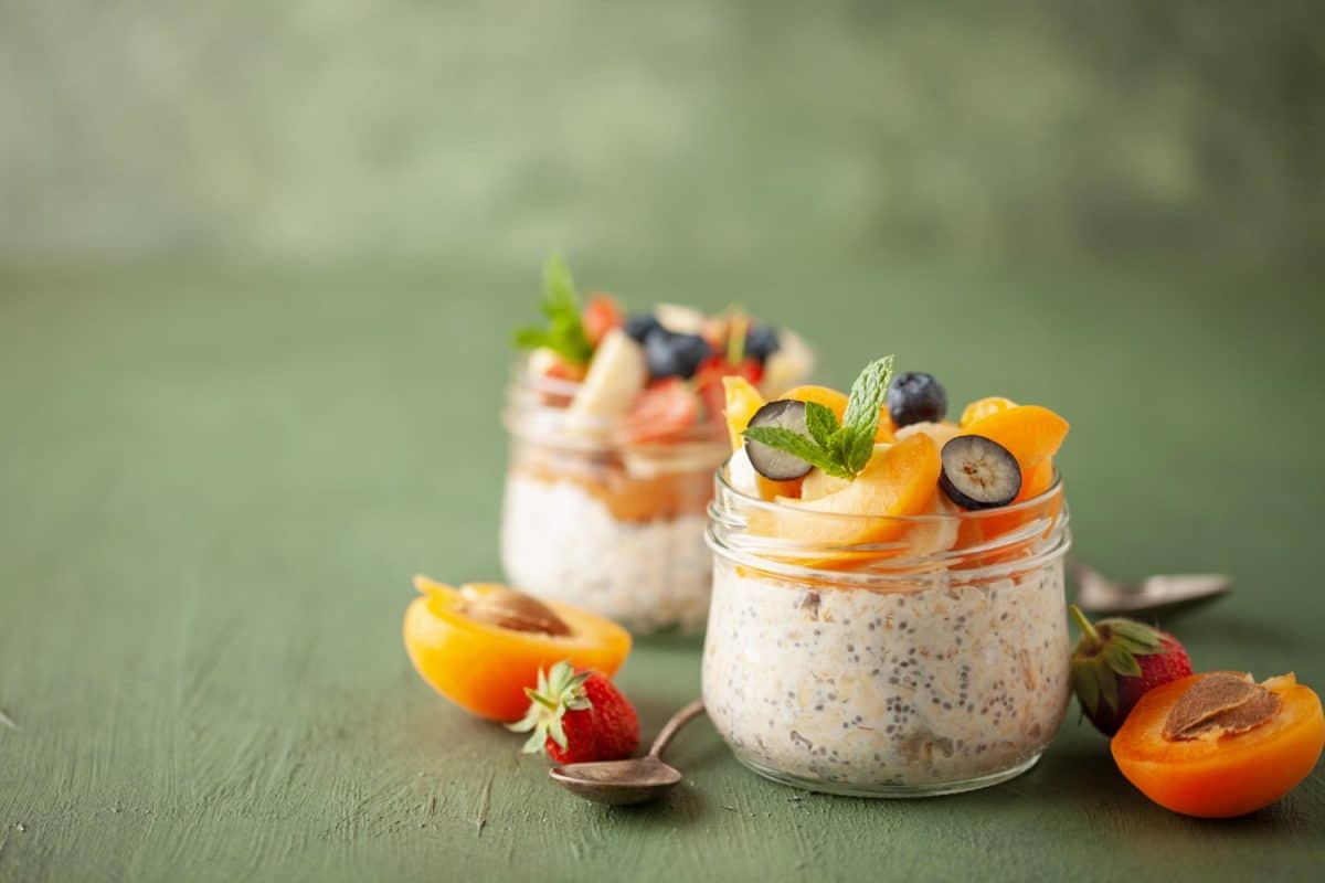Healthy diet breakfast. Overnight oatmeal with chia seeds, bananas, apricot and blueberry in a glass jar on a green wooden background.