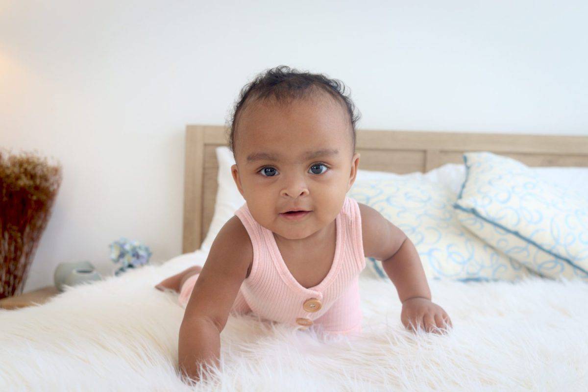 Happy African cute toddle baby infant girl crawling on white bed in bedroom. Portrait of adorable little kid child at home, happy face of child, childhood