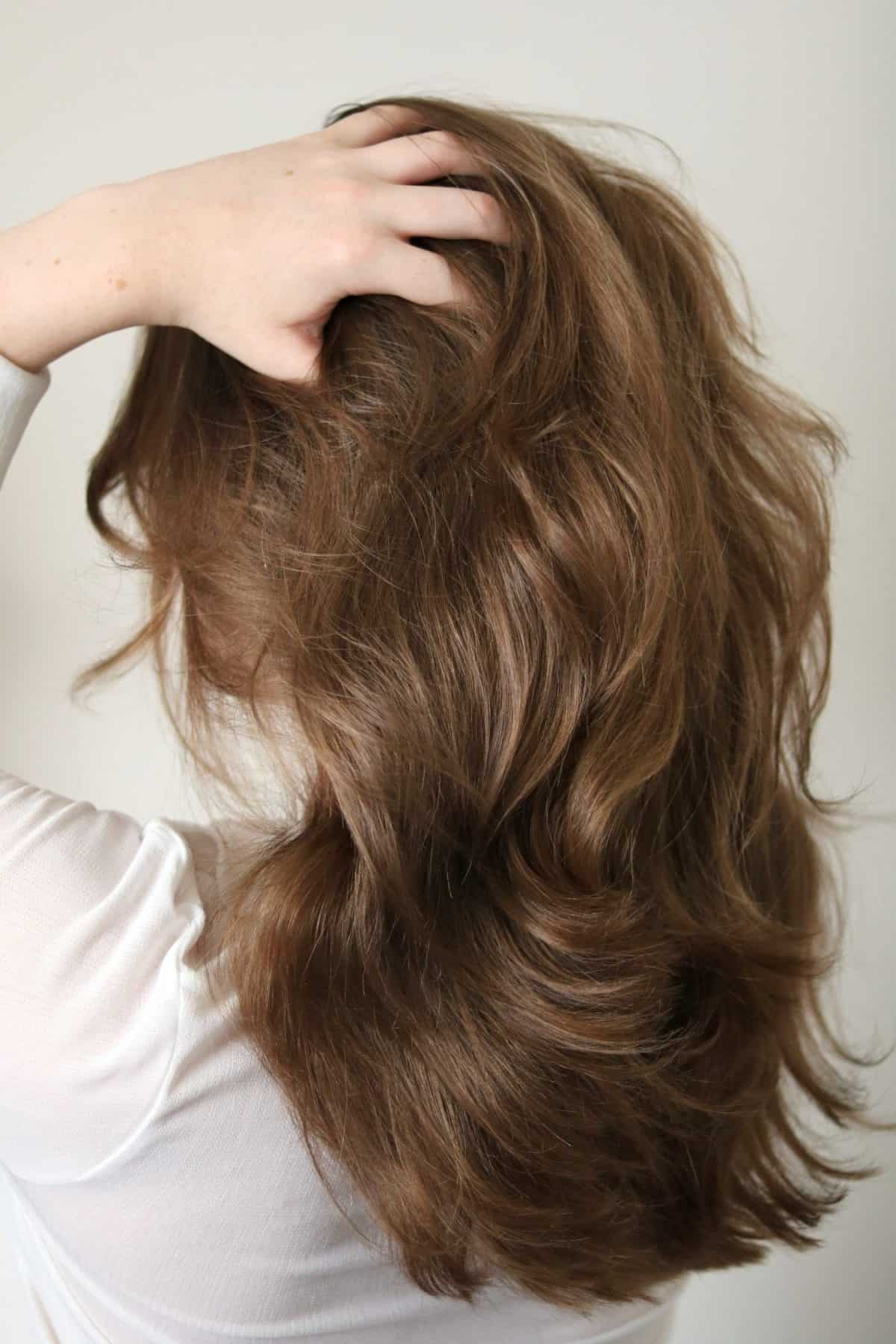 Young woman with long, dark blonde hair running her fingers through hair. New haircut. Playfulness.