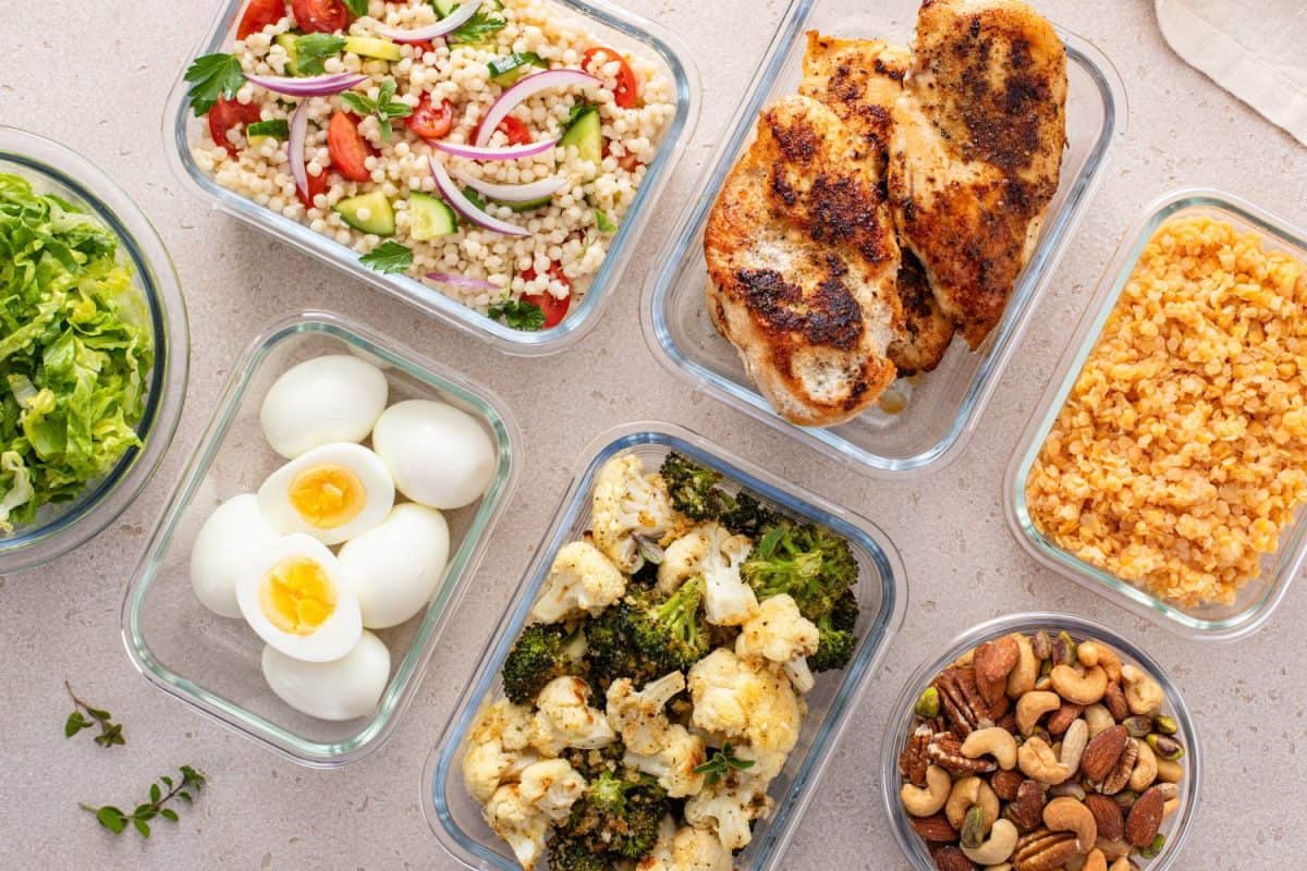 Healthy high protein meal prep with cooked chicken breast, boiled eggs, roasted vegetables, cooked lentils, couscous salad and mixed nuts. Ways to make your hair grow.