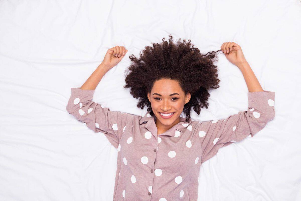 Photo of cute cheerful lady wear pajama lying bed holding hair curls isolated white color background