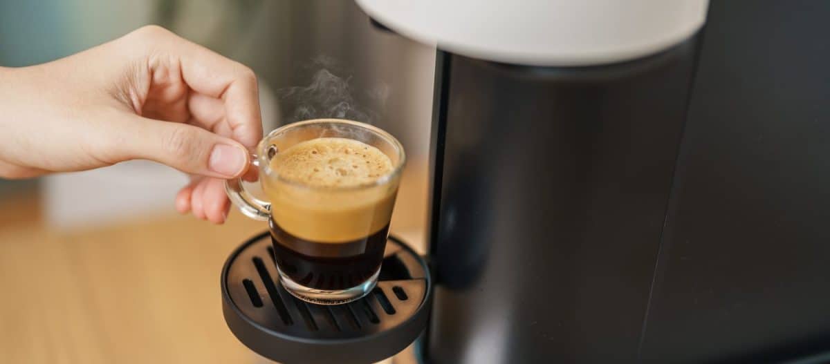 Espresso cup with steam and froth during Coffee making Coffee by Coffee Maker Machine on wood table bar. Cafe shop, Daily beverage drink at Home, Apartment and Office concept