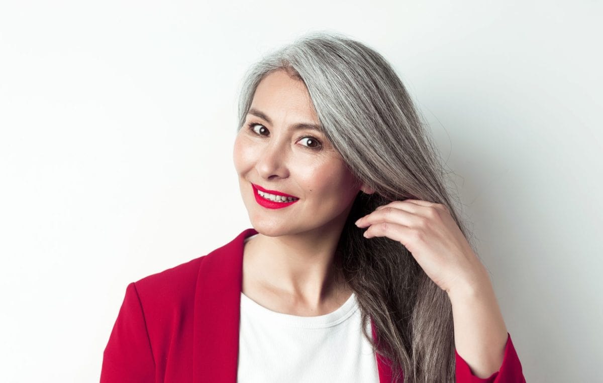 Beauty and haircare concept. Close up of elegant asian senior woman showing shiny and healthy grey hair, smiling and looking aside, white background.