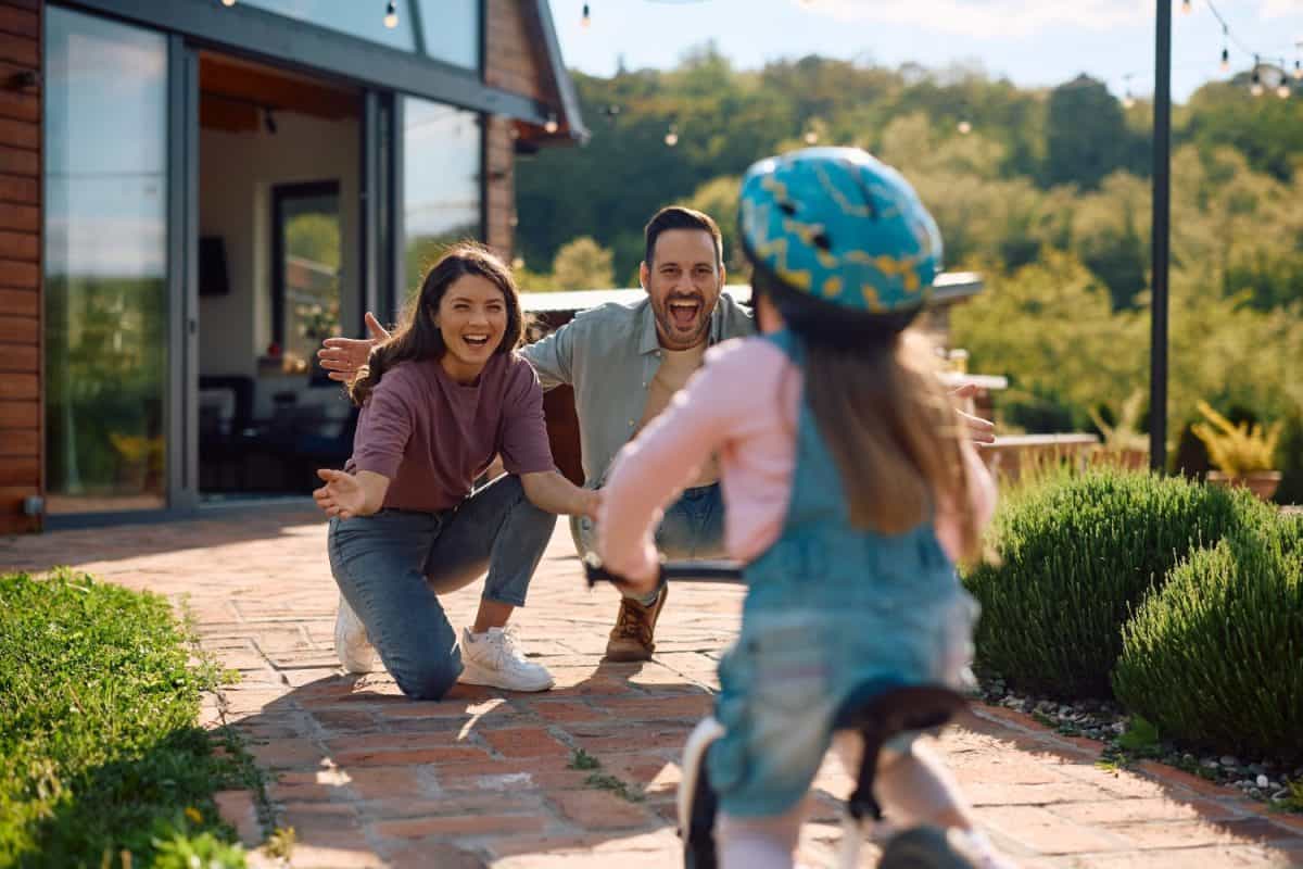 Cheerful parents encouraging their daughter in riding bicycle outdoors. Proven ways to help an anxious child