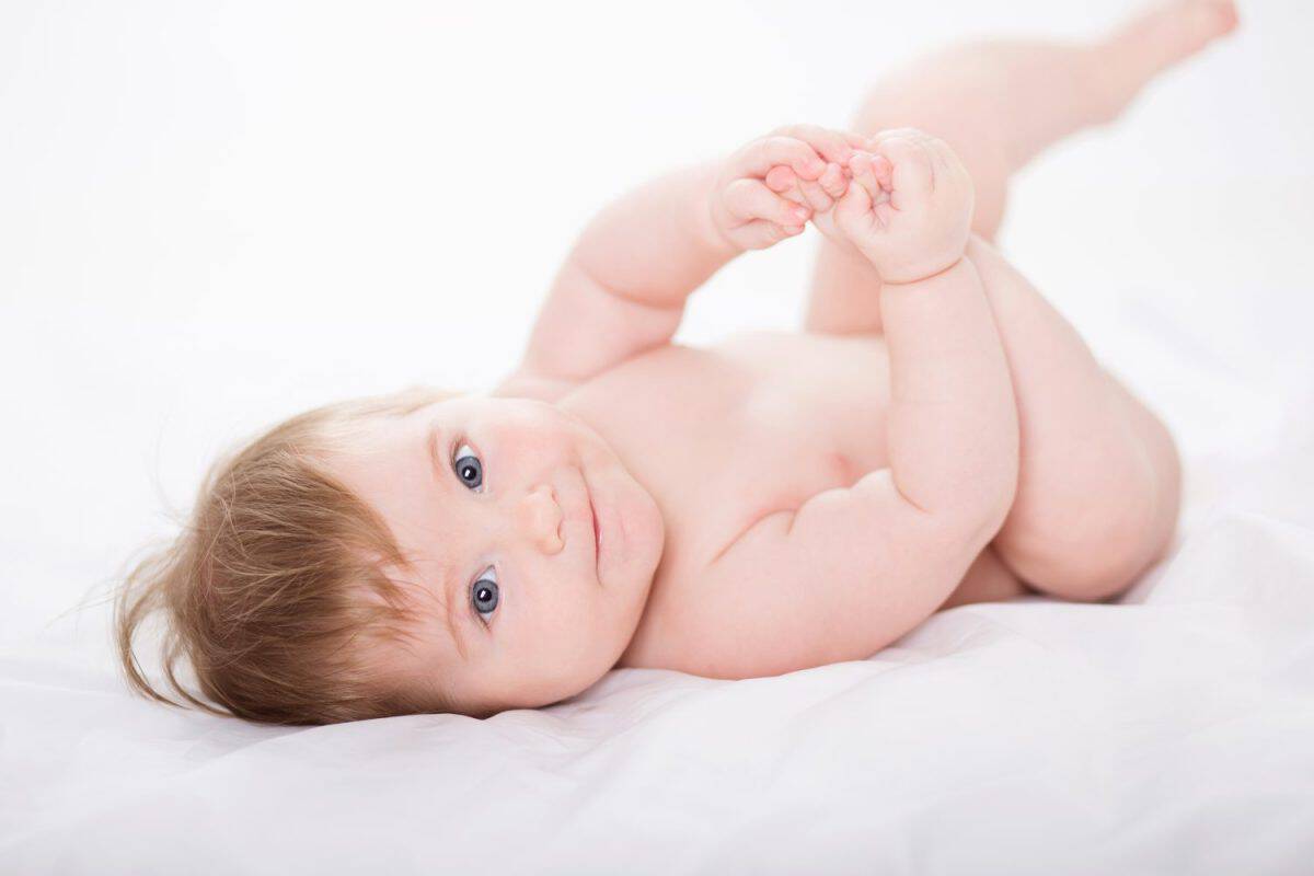 Beautiful smiling baby girl without nappy, lying on a blanket. The best treatment options for diaper rash.