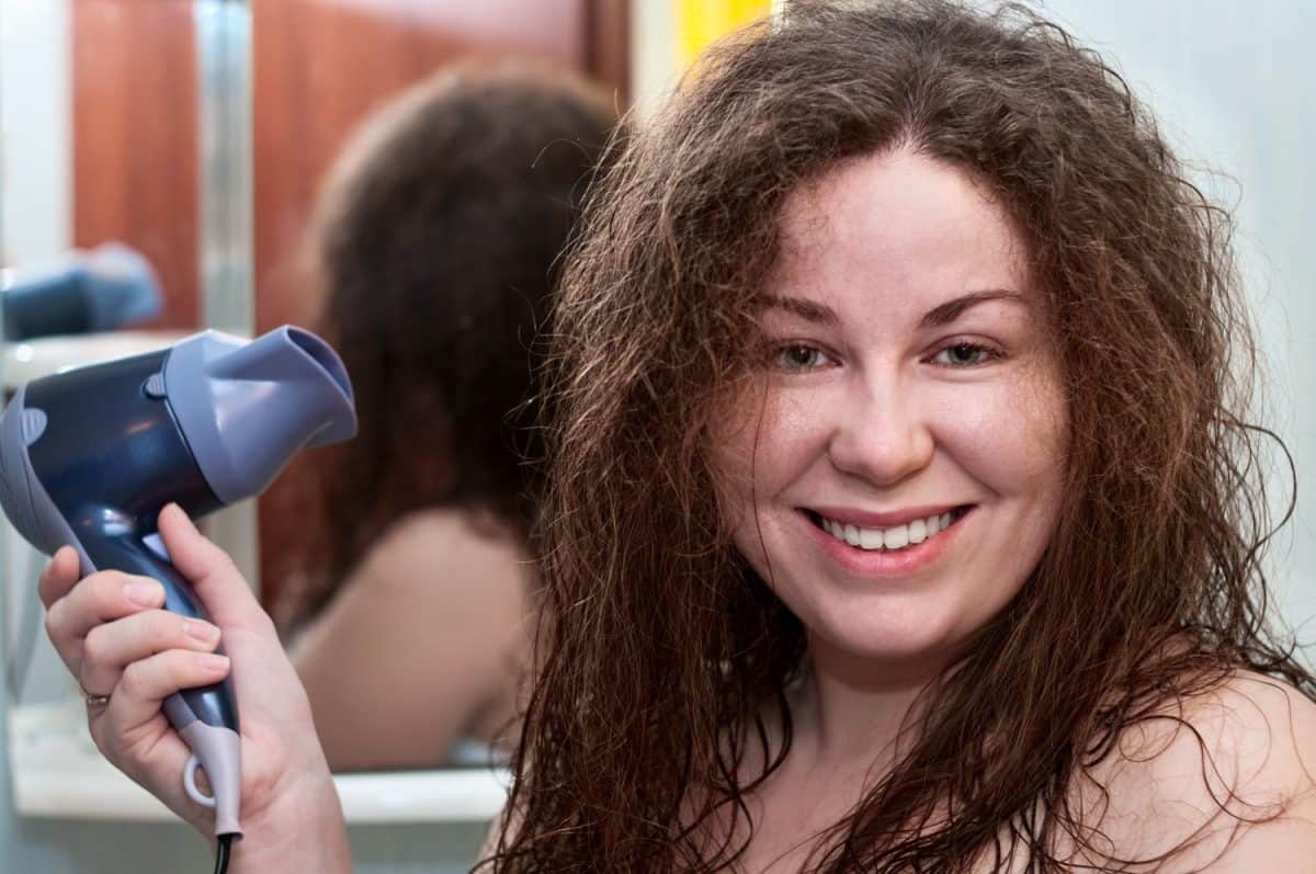 Young caucasian woman with curly brown bushy hair holding hairdryer