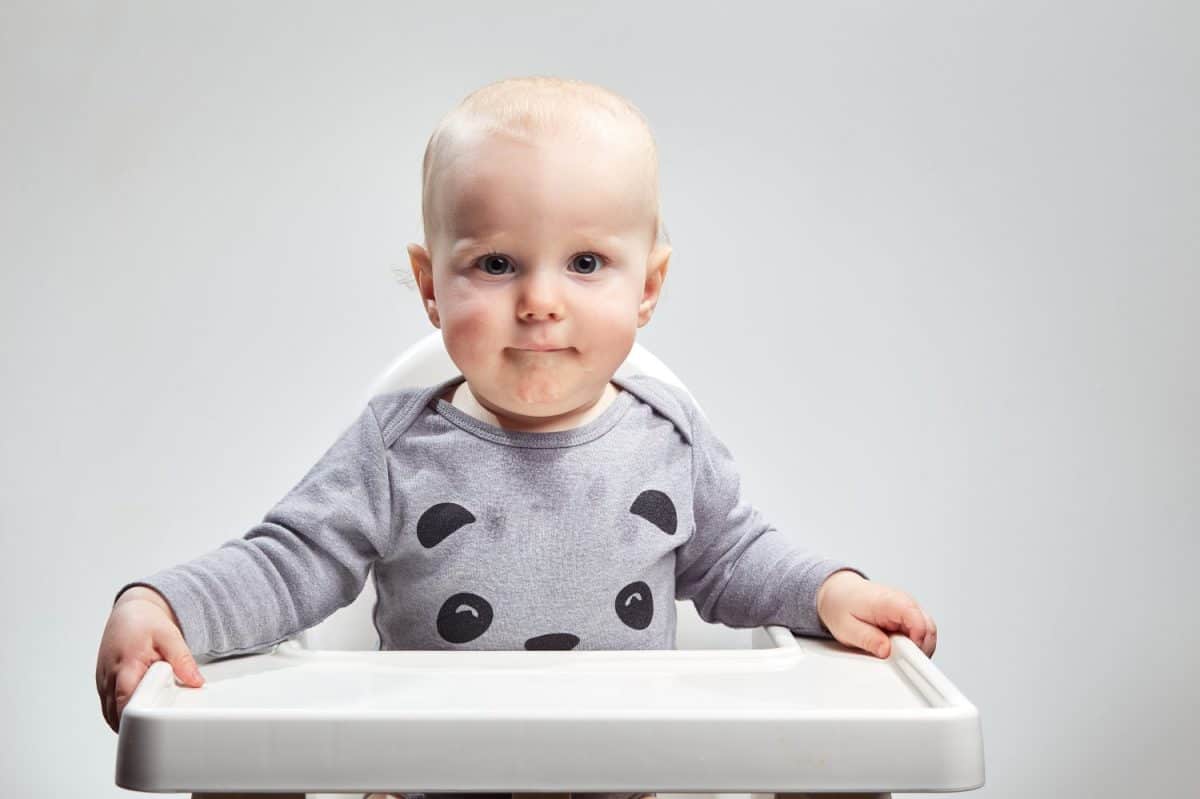 Dramatic caucasian infant sitting straight up in a high chair looking forward on a plain white background. The Best treatment options for croup.