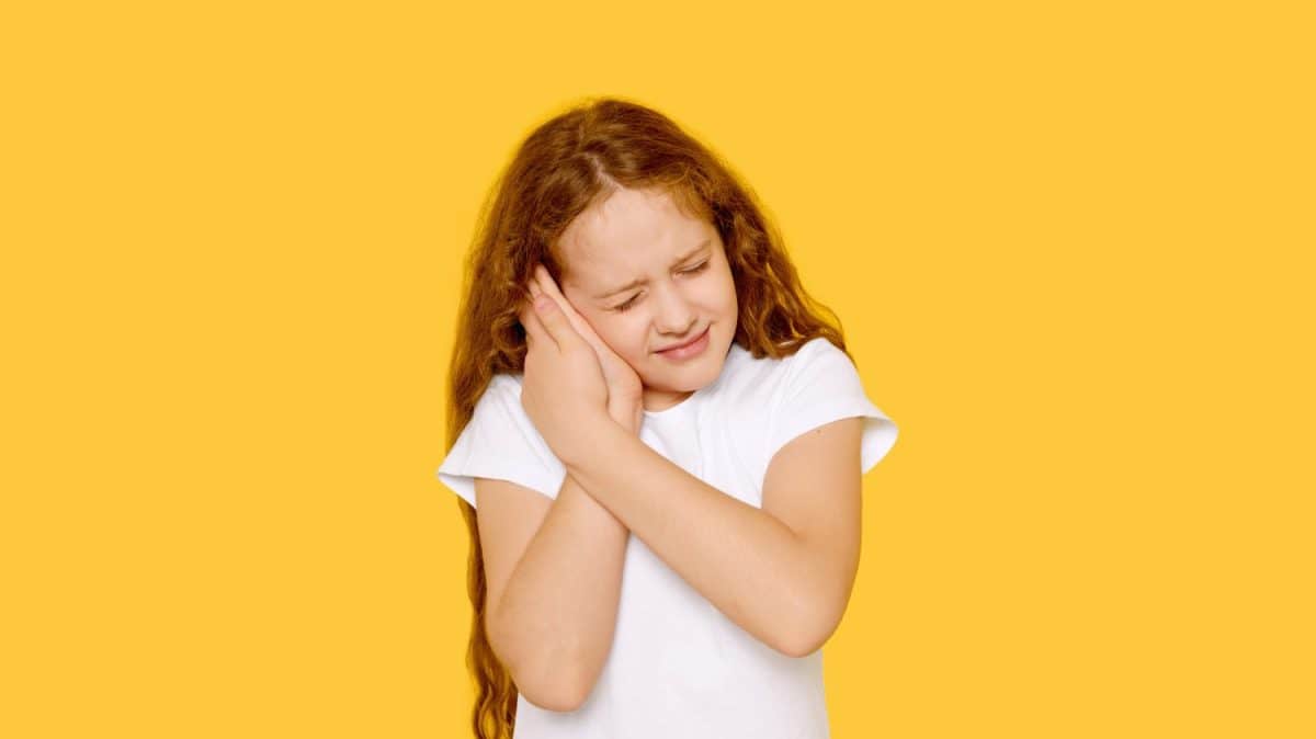 Sad little girl with earache on a yellow background. Ear ache concept. The Most Common Childhood Ailments and How to Treat Them