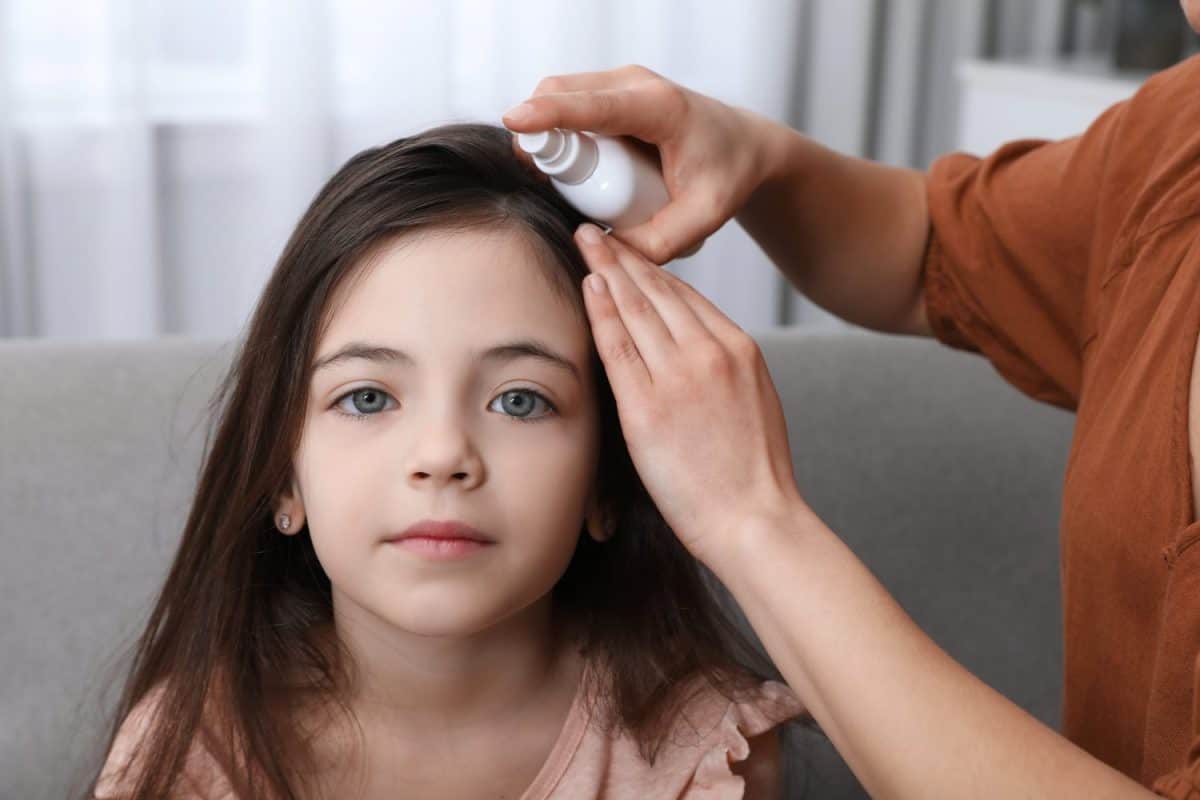 Mother using lice treatment spray on her daughter's hair indoors. The best treatment options for lice.