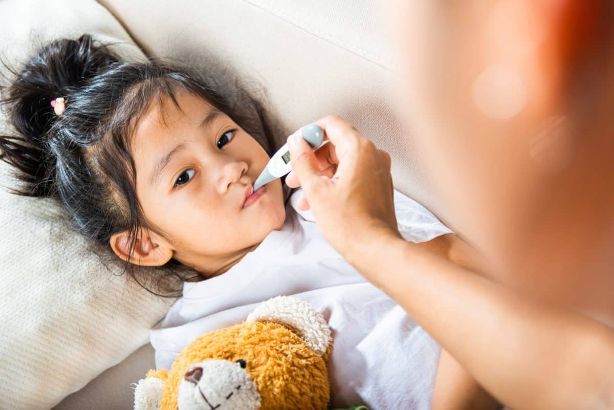 Sick kid. Mother parent checking temperature of her sick daughter with digital thermometer in mouth, child laying in bed taking measuring her temperature for fever and illness, healthcare