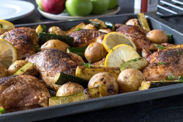 Oven baked chicken legs with potatoes and zucchini on a baking sheet. Served ready to eat on a dining table