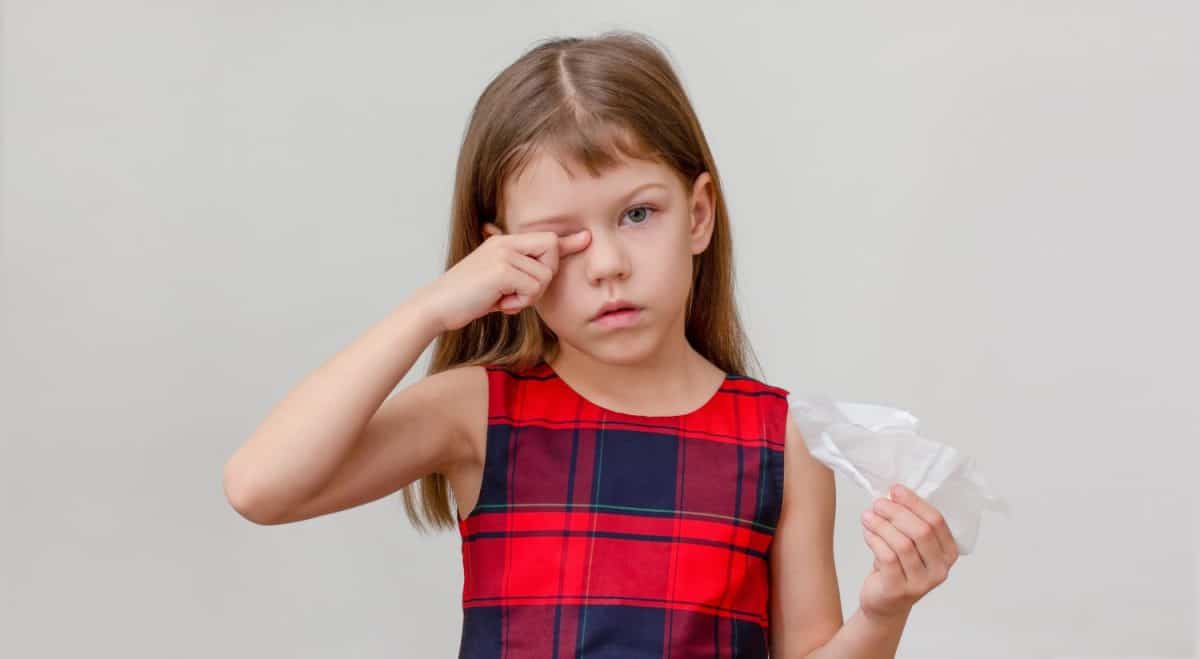 Child scratching eye and holding napkin in hand showing allergy caucasian little girl of 6 7 years on white background looking at camera. The Most Common Childhood Ailments and How to Treat Them