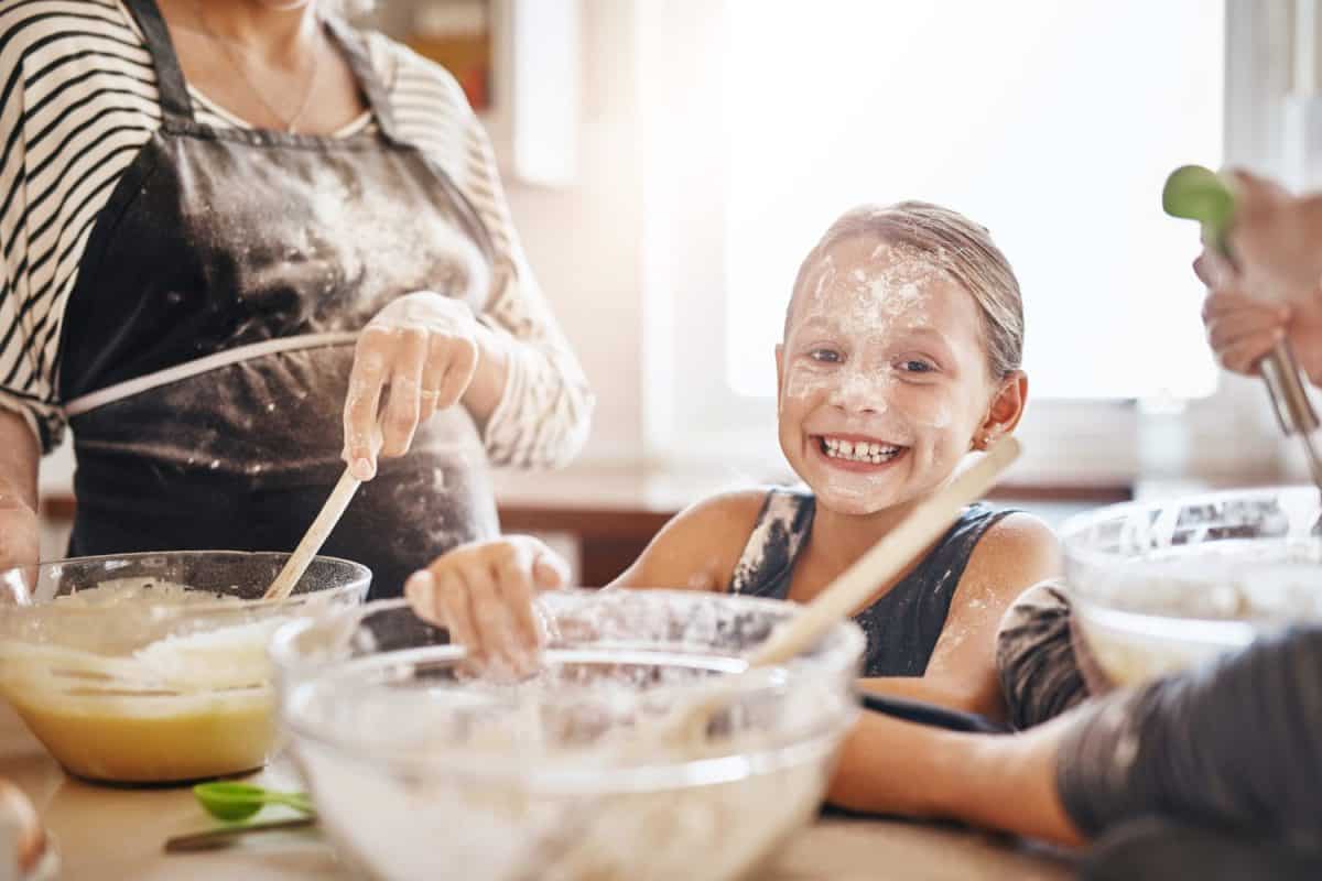 Portrait, playing or messy kid baking in kitchen with a young girl smiling with flour on a dirty face at home. Smile, happy or parent cooking or teaching a fun daughter to bake for child development. The best extra-curricular activities for creative kids.