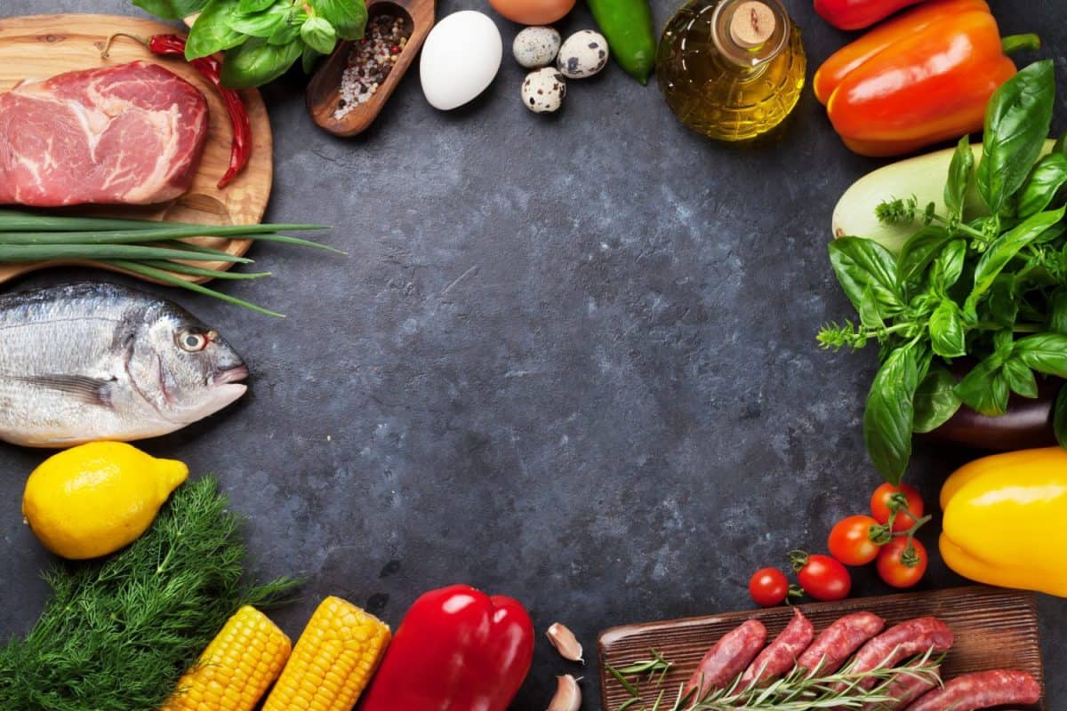 Vegetables, fish, meat and ingredients cooking. Tomatoes, eggplants, corn, beef, eggs. Top view with copy space on stone table