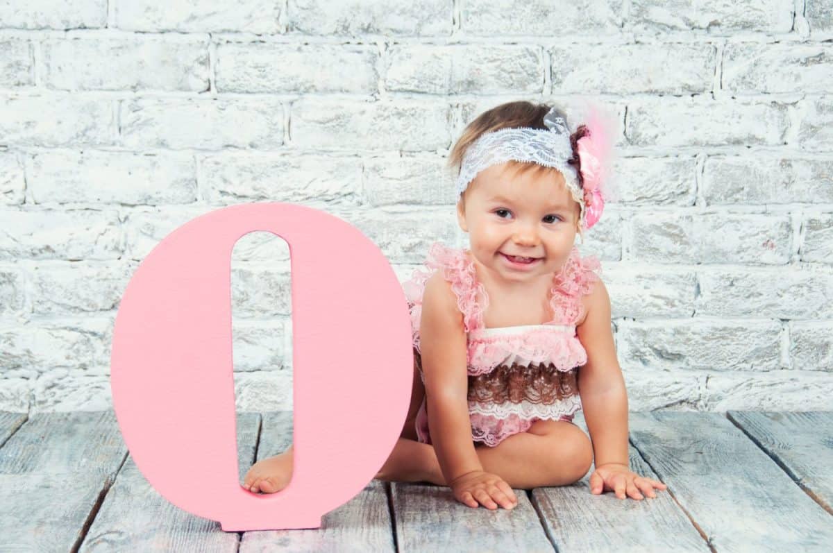 Beautiful and cute girl in a pink dress with the letter O. Emotional girl.