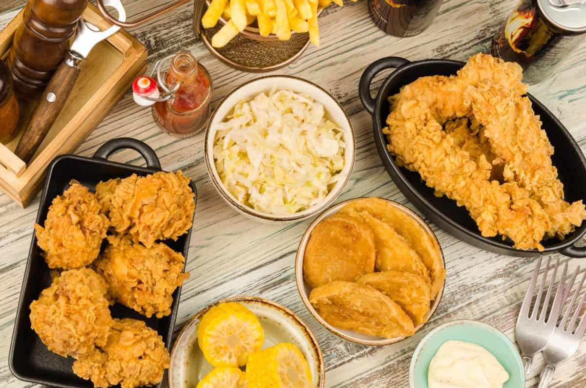 Dinner table with fried chicken wings and strips, roasted potatoes, french fries, coleslaw and sauces. Homemade southern fried chicken. Fried chicken meal